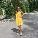 The Amalfi Halter Dress in golden ochre, front view with hand on hip