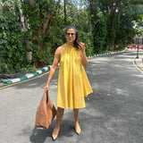 The Amalfi Halter Dress in golden ochre styled with a tan tote bag and nude heels