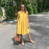 The Amalfi Halter Dress in golden ochre, front view styled with a tan tote bag