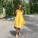 The Amalfi Halter Dress in golden ochre, hands behind back showing the full swing skirt