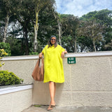 The Daisy Flared Dress in citron yellow, front view leaning against a wall