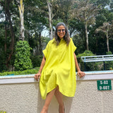 The Daisy Flared Dress in citron yellow, seated on a ledge, front view