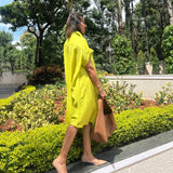 The Daisy Flared Dress in citron yellow, side profile walking with a tote bag